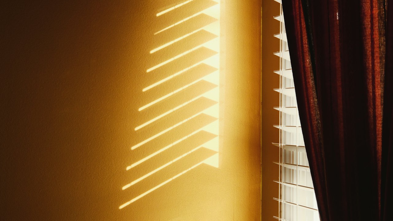Warmes Sonnenlicht fällt durch eine Jalousie auf eine Wand