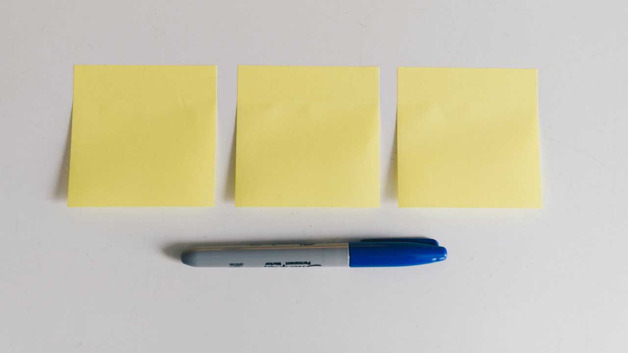 Drei leere gelbe Haftnotizen und ein blauer Marker