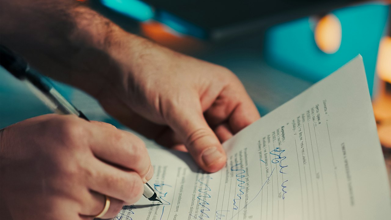 Zwei Hände, eine unterschreibt ein Dokument mit einem Stift